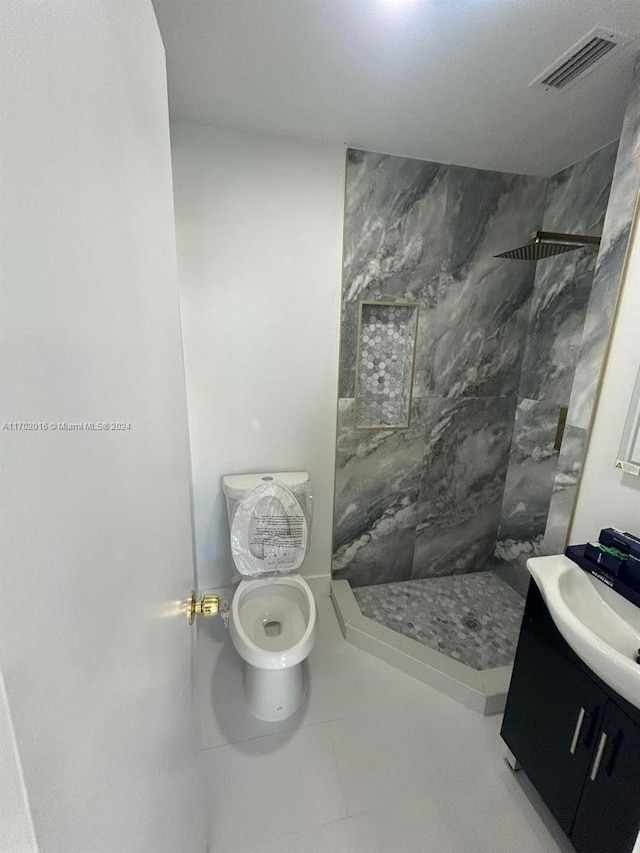 bathroom with a tile shower, vanity, toilet, and tile patterned floors