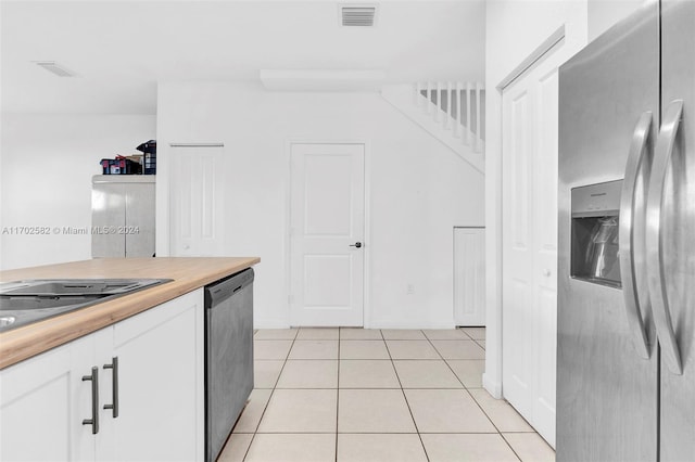 kitchen with appliances with stainless steel finishes, light tile patterned floors, white cabinetry, and butcher block counters