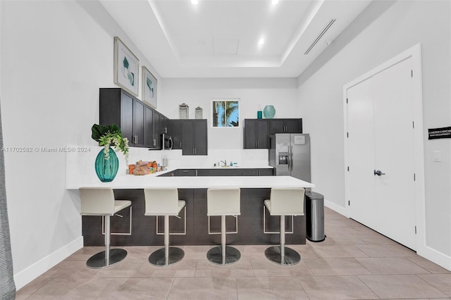 kitchen with a breakfast bar, a raised ceiling, light tile patterned floors, kitchen peninsula, and stainless steel appliances