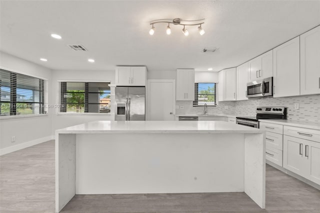 kitchen with white cabinetry, sink, stainless steel appliances, decorative backsplash, and a kitchen island