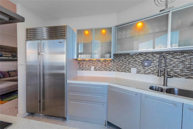 kitchen featuring decorative backsplash, light stone counters, gray cabinetry, sink, and built in refrigerator