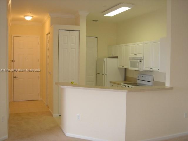 kitchen featuring white cabinetry, kitchen peninsula, crown molding, light colored carpet, and white appliances