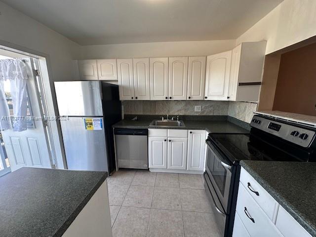 kitchen with backsplash, stainless steel appliances, sink, light tile patterned floors, and white cabinetry