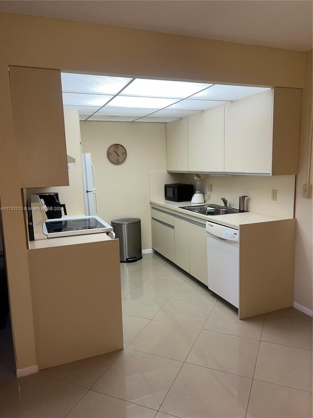 kitchen with light tile patterned flooring, white appliances, sink, and white cabinetry