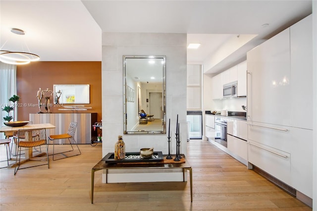 kitchen with appliances with stainless steel finishes, light hardwood / wood-style floors, white cabinetry, and hanging light fixtures