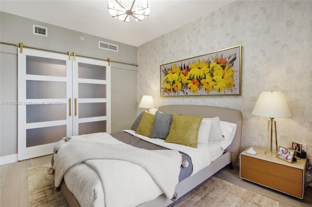 bedroom with hardwood / wood-style flooring, a barn door, and an inviting chandelier