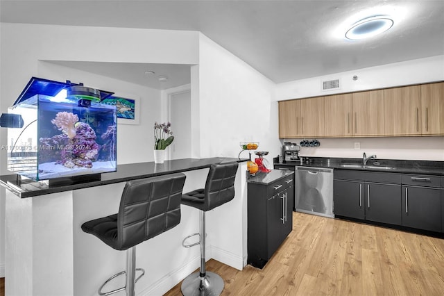 kitchen featuring sink, a kitchen breakfast bar, stainless steel dishwasher, dark stone countertops, and light wood-type flooring