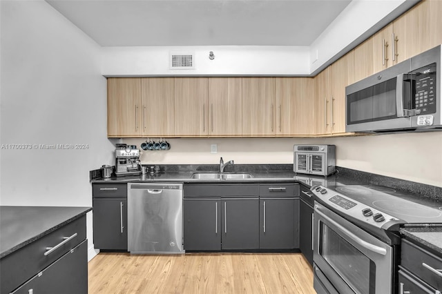 kitchen featuring stainless steel appliances, light hardwood / wood-style flooring, dark stone counters, and sink