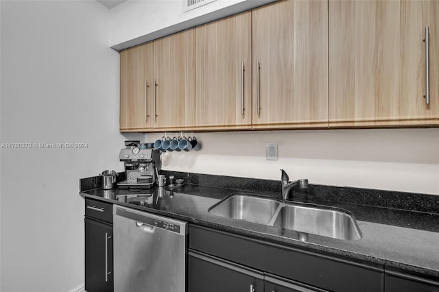 kitchen with light brown cabinets, stainless steel dishwasher, dark stone countertops, and sink