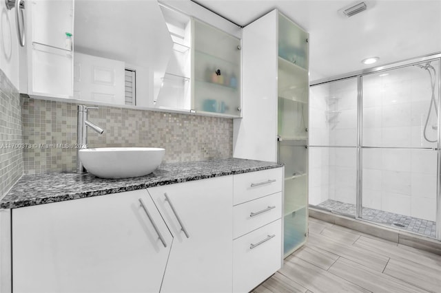 bathroom featuring vanity, decorative backsplash, and a shower with door