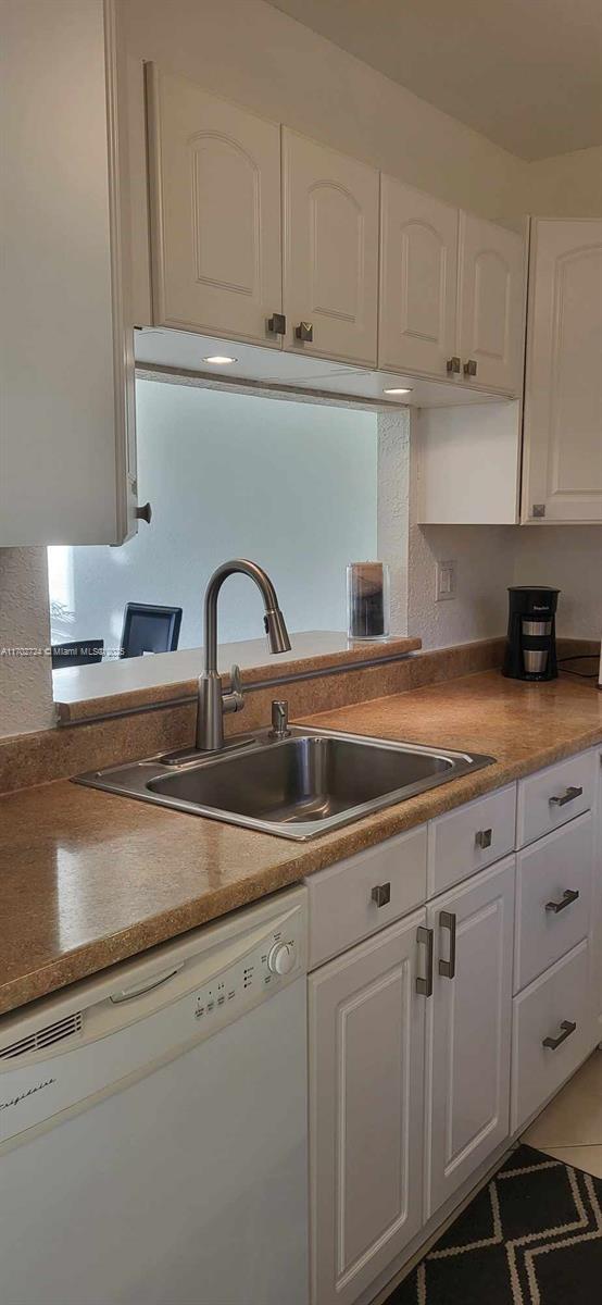 kitchen with dark tile patterned floors, dishwasher, white cabinets, and sink