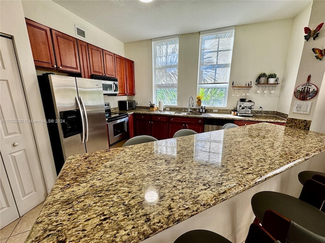 kitchen featuring light stone counters, kitchen peninsula, a textured ceiling, a breakfast bar, and appliances with stainless steel finishes