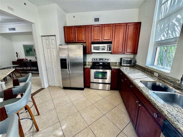 kitchen with dark stone countertops, sink, light tile patterned flooring, and stainless steel appliances