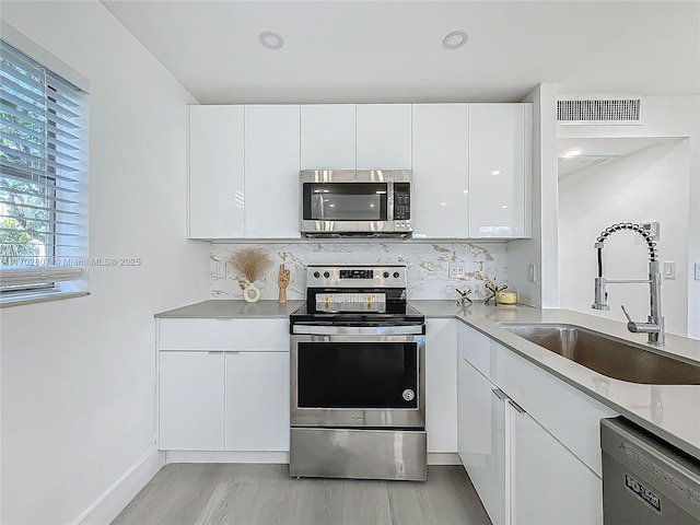 kitchen featuring stainless steel appliances, a sink, white cabinetry, tasteful backsplash, and light countertops