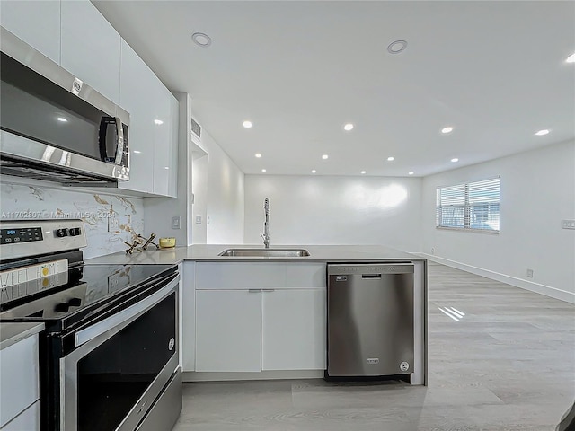 kitchen with white cabinetry, sink, stainless steel appliances, backsplash, and kitchen peninsula