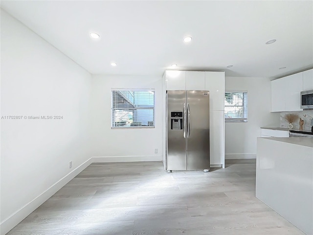 kitchen with white cabinets, appliances with stainless steel finishes, light hardwood / wood-style floors, and a wealth of natural light