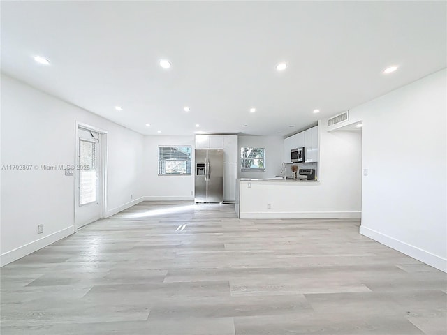 unfurnished living room featuring recessed lighting, baseboards, light wood-type flooring, and a sink