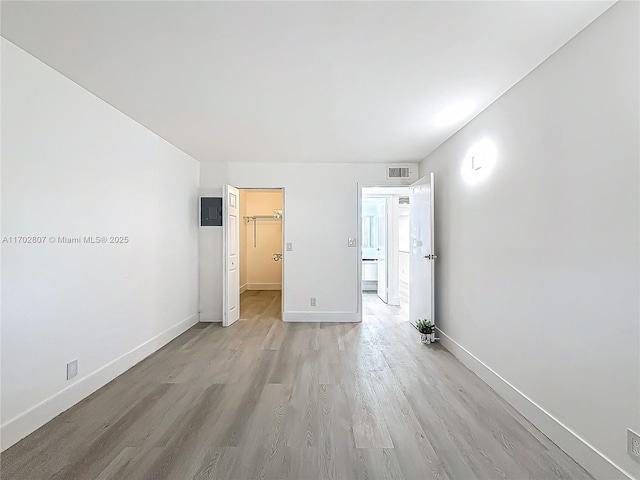 unfurnished bedroom featuring light wood-style flooring, baseboards, and a spacious closet