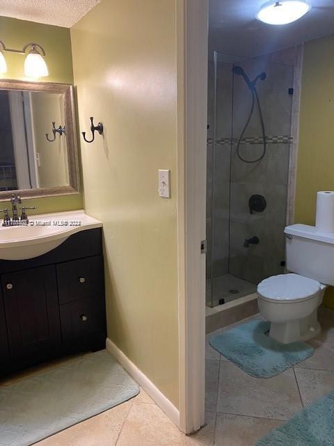 bathroom featuring a tile shower, vanity, a textured ceiling, tile patterned flooring, and toilet