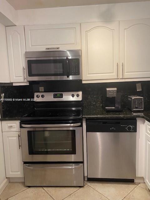 kitchen featuring tasteful backsplash, white cabinetry, light tile patterned flooring, and stainless steel appliances