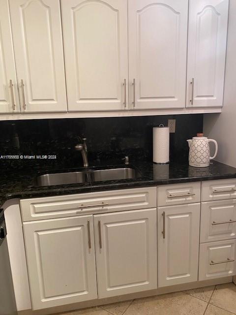 kitchen featuring sink, light tile patterned floors, dark stone counters, decorative backsplash, and white cabinets