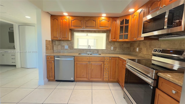 kitchen with stainless steel appliances, sink, light tile patterned floors, and light stone counters