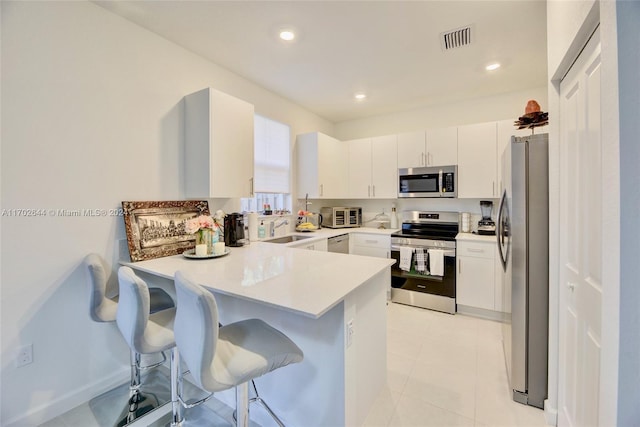 kitchen with white cabinets, appliances with stainless steel finishes, a kitchen bar, and kitchen peninsula