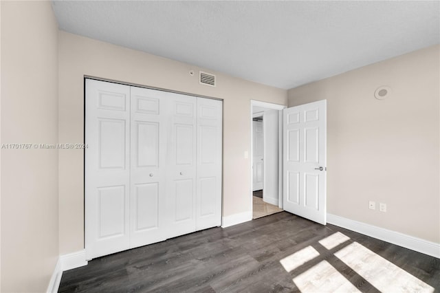 unfurnished bedroom with a textured ceiling, dark wood-type flooring, and a closet