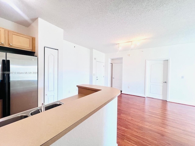 kitchen with a textured ceiling, stainless steel refrigerator, light brown cabinetry, and dark hardwood / wood-style flooring