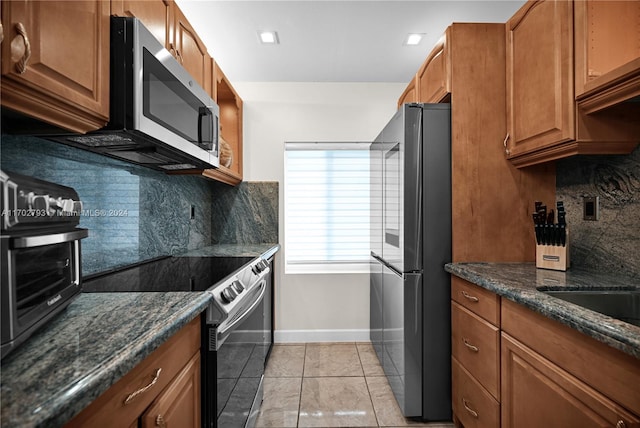 kitchen featuring dark stone counters, decorative backsplash, light tile patterned floors, and stainless steel appliances