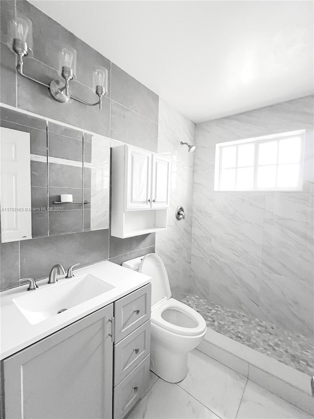 bathroom with vanity, tiled shower, tile walls, and toilet