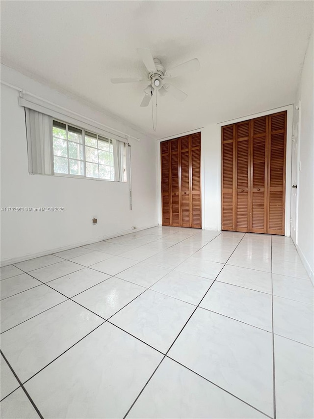 unfurnished bedroom featuring ceiling fan, light tile patterned floors, and two closets