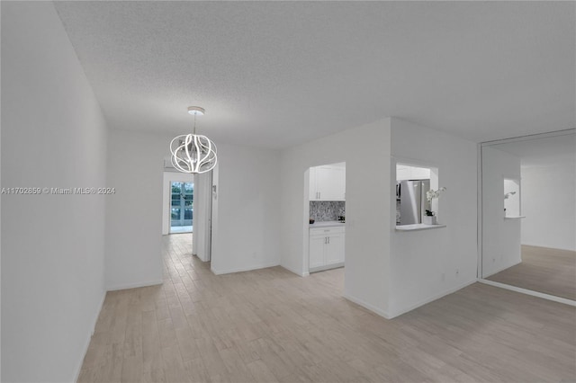 empty room with a textured ceiling, light wood-type flooring, and an inviting chandelier