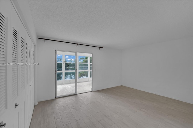 unfurnished bedroom featuring a water view, a textured ceiling, and access to outside