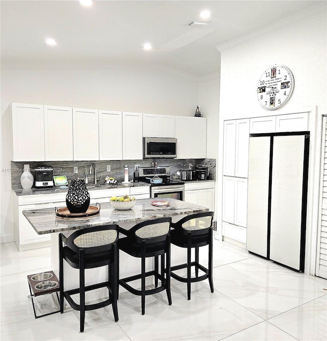 kitchen with light stone countertops, a kitchen island, vaulted ceiling, white cabinets, and appliances with stainless steel finishes