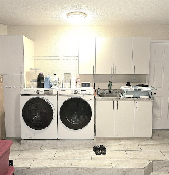 washroom with cabinets, a textured ceiling, washer and clothes dryer, and sink