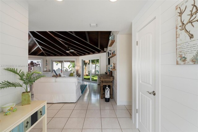 hall featuring light tile patterned floors, lofted ceiling, and wood walls