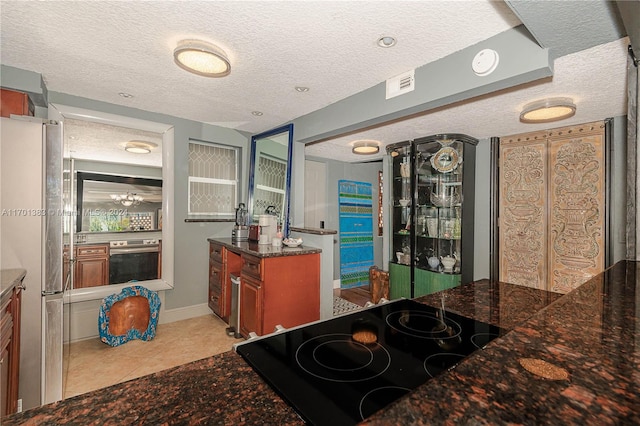 kitchen with a textured ceiling, dark stone countertops, light tile patterned floors, and stainless steel appliances