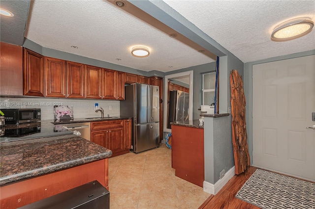 kitchen featuring sink, stainless steel appliances, dark stone countertops, a textured ceiling, and decorative backsplash