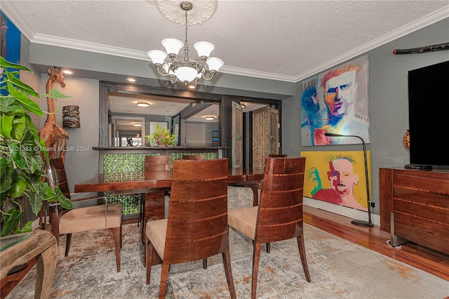 dining area featuring crown molding, wood-type flooring, a textured ceiling, and an inviting chandelier