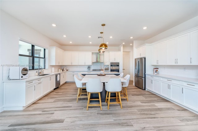 kitchen with wall chimney exhaust hood, sink, a center island, and appliances with stainless steel finishes