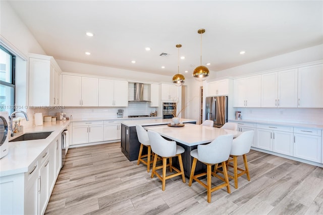 kitchen with a center island, wall chimney exhaust hood, hanging light fixtures, stainless steel appliances, and a kitchen bar