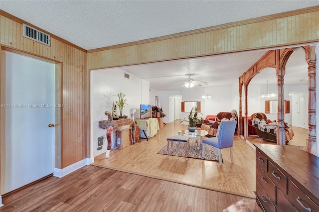 living room featuring ceiling fan with notable chandelier, light wood-type flooring, and a textured ceiling