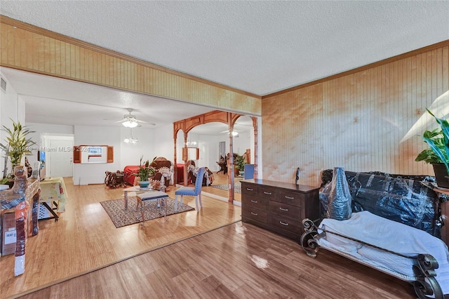 living room with a textured ceiling, light hardwood / wood-style floors, ceiling fan, and crown molding