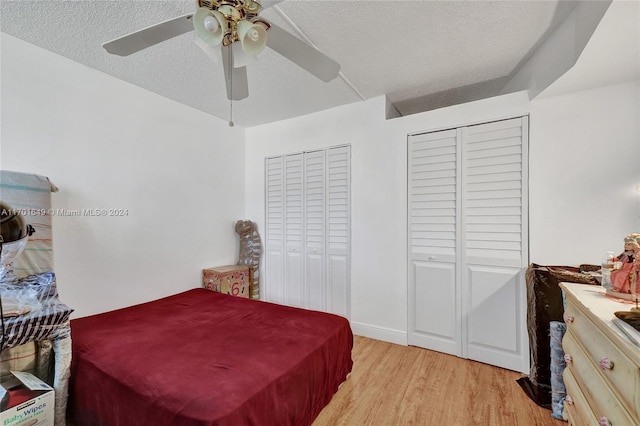 bedroom with a textured ceiling, two closets, light hardwood / wood-style flooring, and ceiling fan