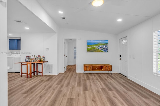 foyer entrance featuring light wood-type flooring, washer and clothes dryer, vaulted ceiling, and plenty of natural light