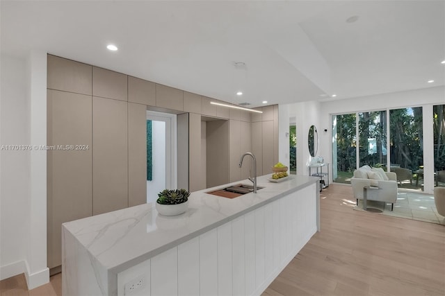 kitchen featuring gray cabinetry, light stone counters, a center island with sink, and light hardwood / wood-style floors