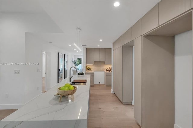 kitchen with decorative backsplash, light wood-type flooring, light stone counters, sink, and gray cabinets