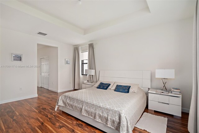 bedroom featuring a raised ceiling and dark wood-type flooring