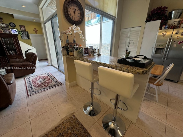 kitchen featuring dark stone counters, stainless steel fridge, light tile patterned floors, a kitchen bar, and kitchen peninsula